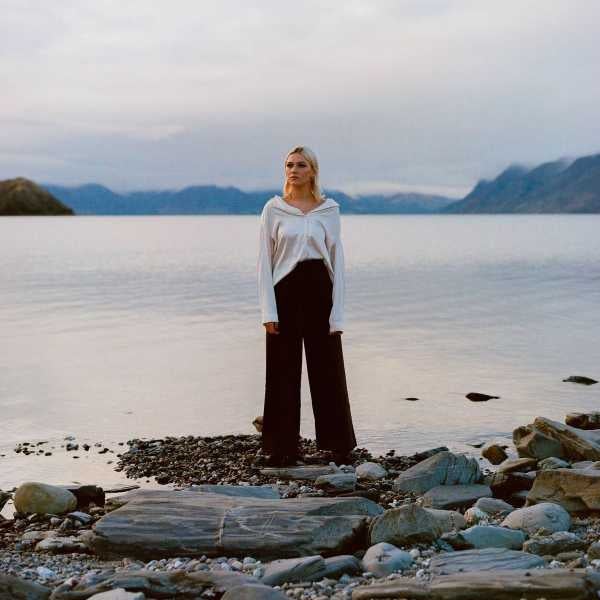 Photo of a female musician standing on a rock near the edge of a lake