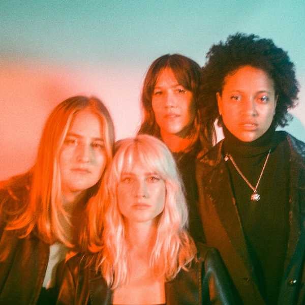 Photo of four female musicians staring into the camera with a bright orange light over their faces