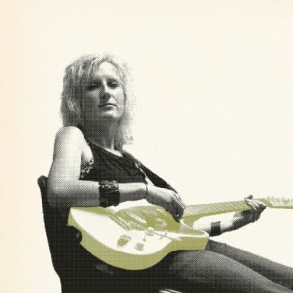 Photo of female artist Mia Dyson sitting in a chair holding an electric guitar 