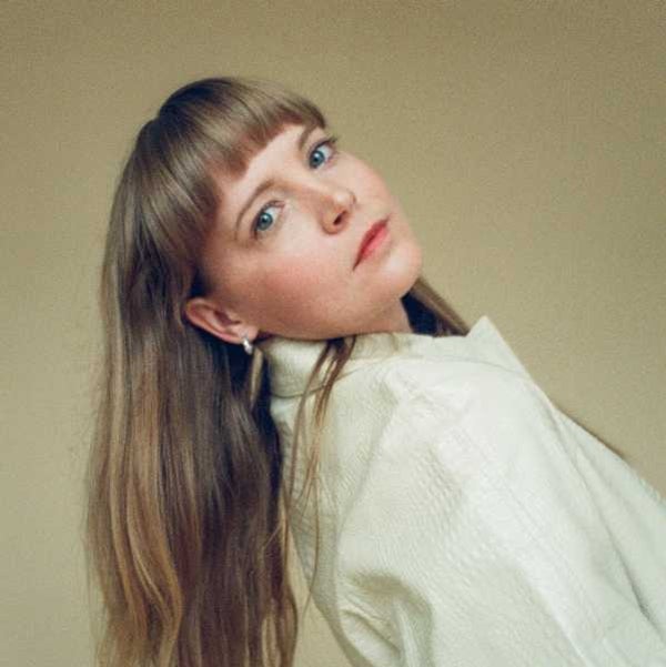 Photo of female musician leaning her head to the side. She has long light brown hair and a front fringe