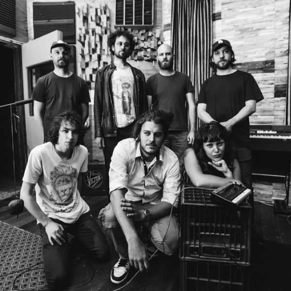 Black and white photo of 7-piece band Seven Ups standing infront of a brick wall
